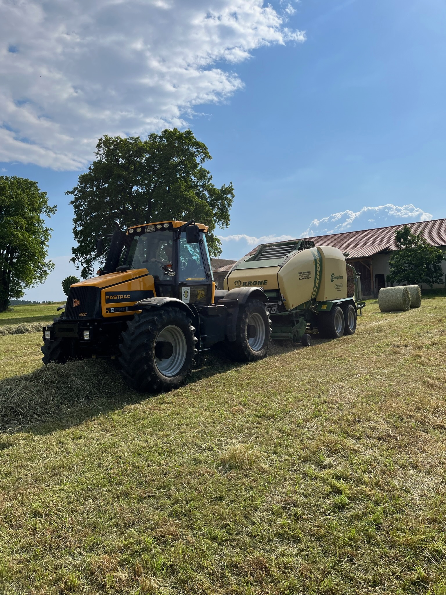 JCB-Traktor mit Krone-Comprima-Rundballenpresse auf einer Wiese